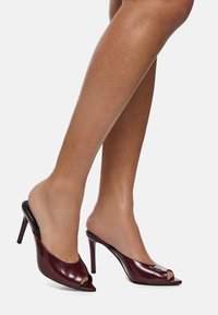 Burgunderfarbene Lackleder-Pumps mit offenem Zeh, die eine elegante Silhouette und ein rückenloses Design aufweisen. Glatte, glänzende Oberfläche.