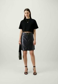 T-shirt cropped preto, saia de ganga escura de cintura alta com fecho na frente, sandálias altas pretas, e uma bolsa preta brilhante.