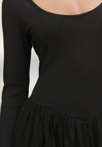 Fekete ruha bordázott textúrával a felső részen, alakot követő felső résszel, mély kivágással és buggyos, bő szoknyával.