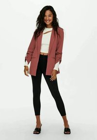 Pink blazer with structured design, open front, paired with a white top, black leggings, and black slide sandals. Textured fabric and tailored fit.