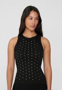 Débardeur noir en ribbed avec des clous carrés argentés disposés en motif quadrillé, col montant et sans manches.