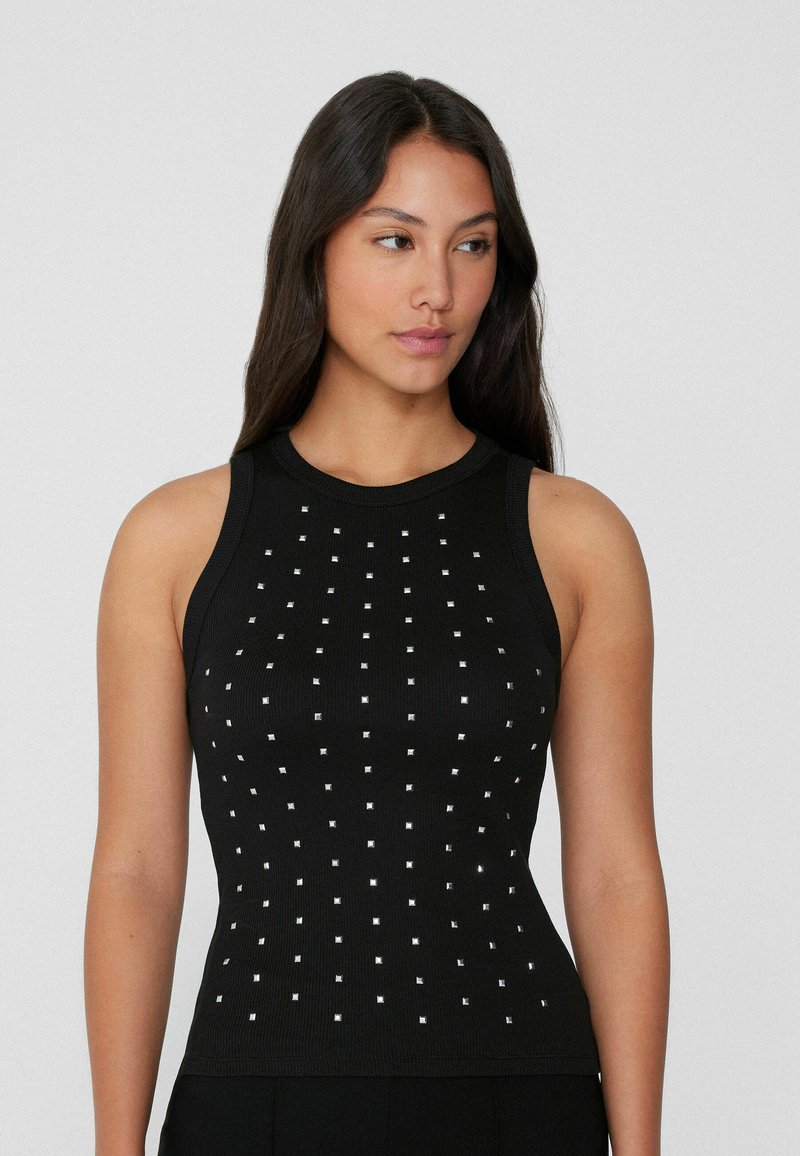 Débardeur noir en ribbed avec des clous carrés argentés disposés en motif quadrillé, col montant et sans manches.
