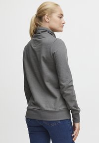 Felpa grigia con colletto alto, maniche lunghe e vita aderente. Texture liscia e design semplice, abbinata a jeans blu scuro.