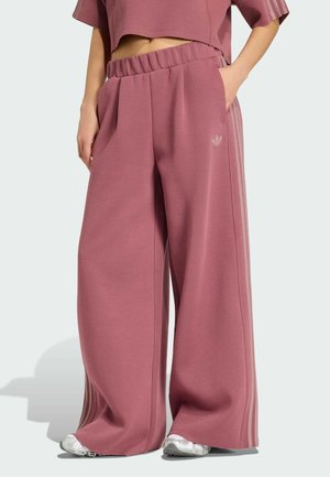 Vidde mauve træningsbukser med elastisk talje og sidelommer, båret med sølv sneakers, hånd i lommen, synlig cropped mauve top.