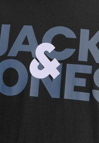Suur, julge sinine kiri "JACK & JONES" mustal kangasel taustal, valge ampersandi sümbol on teksti kohal.