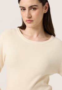Hellbeige geripptes Sweatshirt mit weitem Ausschnitt. Weiche Textur und taillierte Silhouette, minimalistisches Design ohne Muster oder Verzierungen.