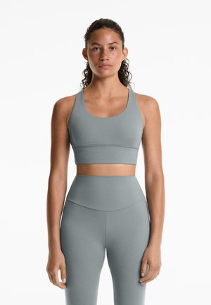 Light gray sports bra with wide straps and a scoop neckline, paired with matching high-waisted leggings in a smooth, stretchy fabric.