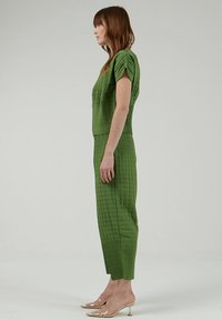 Conjunto de dos piezas texturizado en verde que presenta un top acolchado con mangas dobladas y pantalones ajustados. Estilo claro y silueta ceñida. Tacones transparentes.