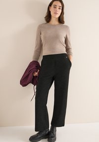 Pantalons noirs à jambe large texturés avec une taille ajustée, associés à un haut beige à manches longues et une veste bordeaux portée sur un bras.