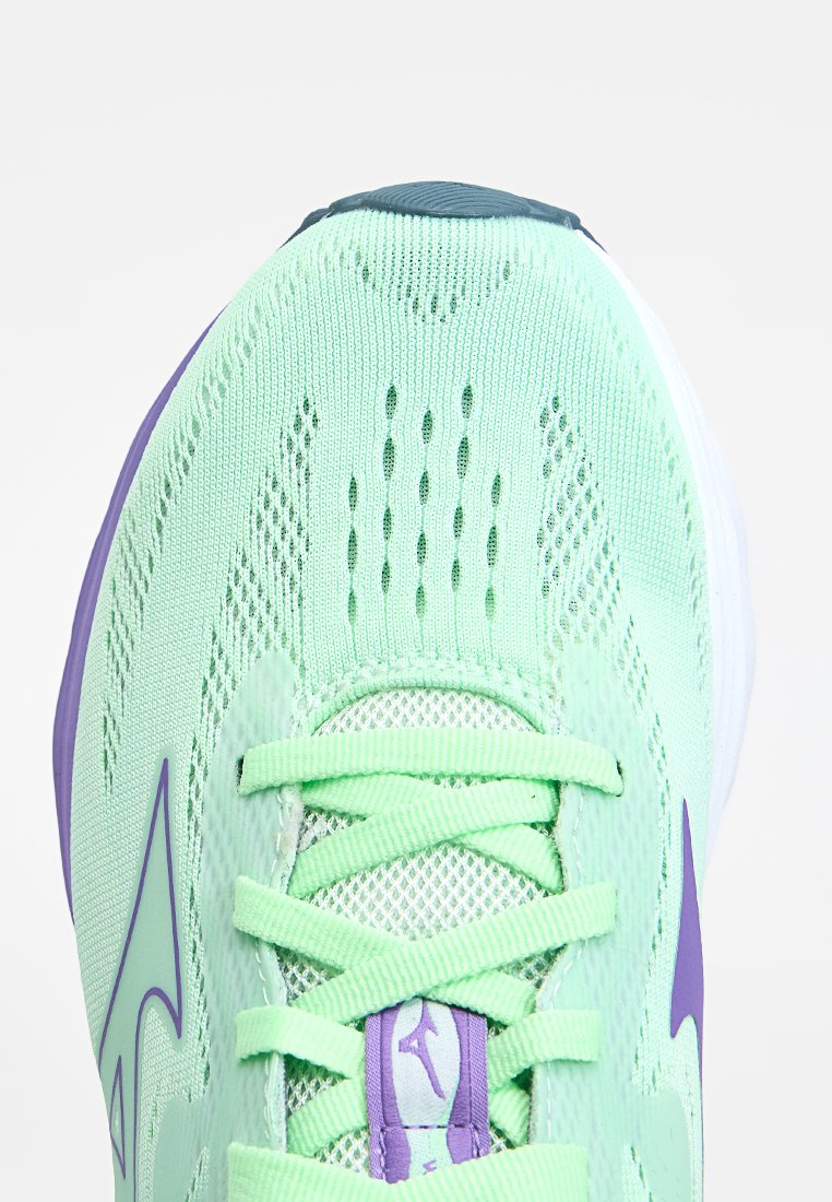 Zapatilla de running verde claro con parte superior de malla, superficie texturizada, acentos morados y cordones planos. Presenta agujeros de ventilación y talón reforzado.