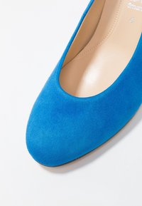 Blue suede ballet flat with a rounded toe, smooth interior, and light tan sole. No hardware or embellishments. Classic design.