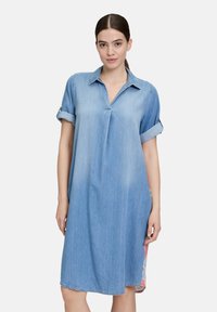 Sukienka koszulowa z dżinsu, z kołnierzykiem, podwiniętymi rękawami i luźnym fasonem. Jasnoniebieski kolor z delikatnym wyblaknięciem i postrzępionymi brzegami. Akcent w formie bocznego kwiatowego nadruku.