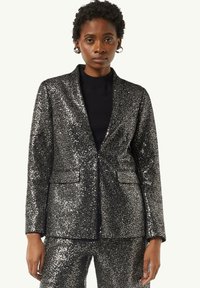 Czarna blazerka z cekinami o dopasowanym kroju, z klapkami i dwoma przednimi kieszeniami. W komplecie z czarną bluzką pod spodem.