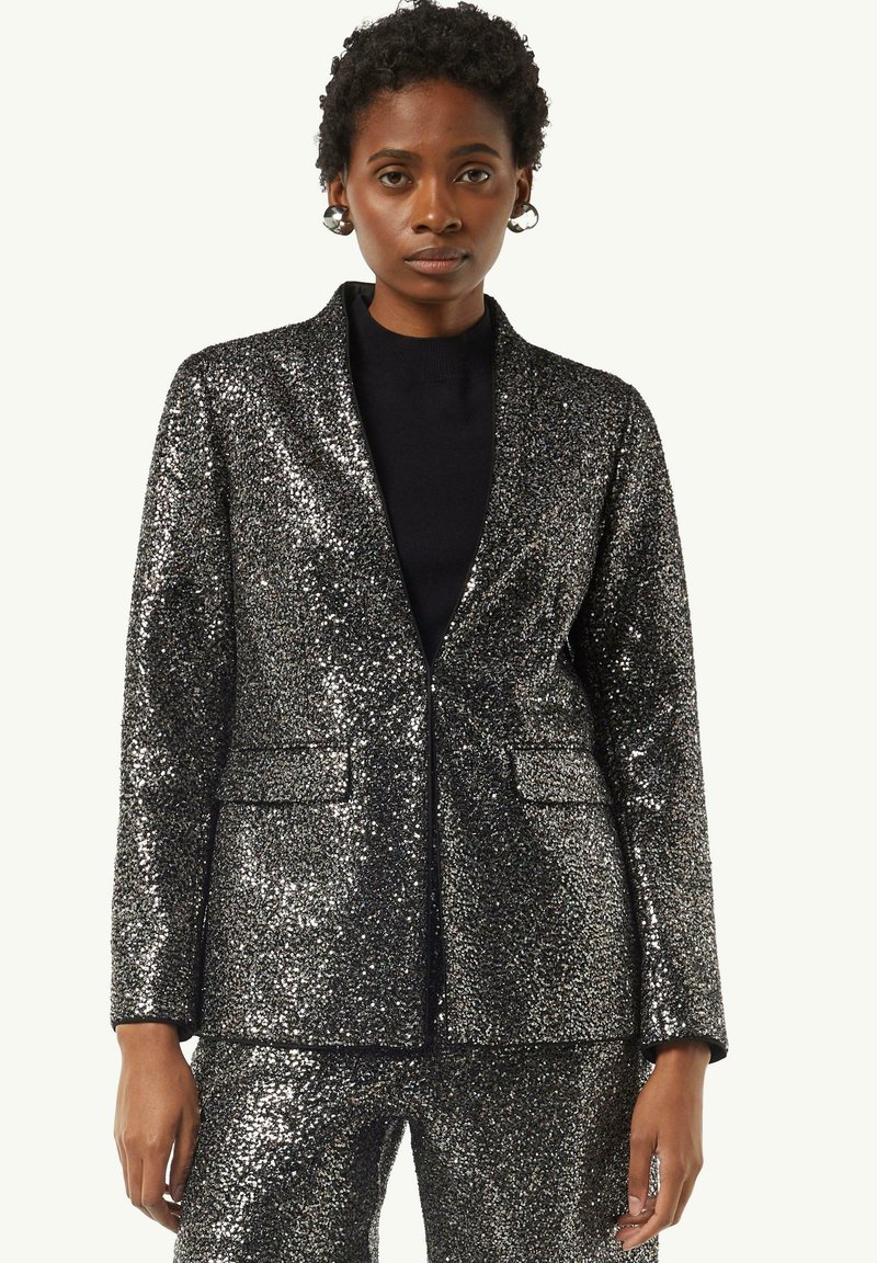 Czarna blazerka z cekinami o dopasowanym kroju, z klapkami i dwoma przednimi kieszeniami. W komplecie z czarną bluzką pod spodem.