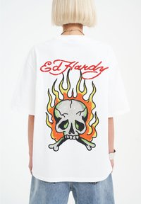 Bílé oversized tričko s barevným designem lebky a plameny, červeným textem "Ed Hardy" a volným střihem. Měkký bavlněný materiál.