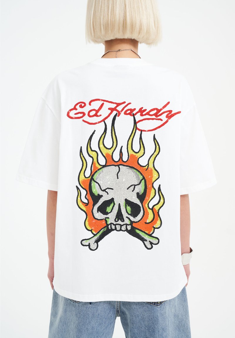 Bílé oversized tričko s barevným designem lebky a plameny, červeným textem "Ed Hardy" a volným střihem. Měkký bavlněný materiál.
