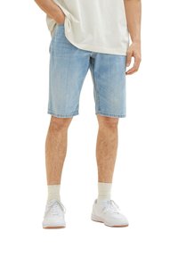 Pantalones cortos de mezclilla azul claro con un corte relajado, bordes deshilachados y bolsillos laterales, combinados con zapatillas blancas y calcetines color crema.