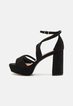 Μαύρες σουέτ σανδάλια με πλατφόρμα και χοντρό τακούνι, με ενωμένες λωρίδες και λουράκι με πόρπη στον αστράγαλο. Υφή επιφάνειας και σύγχρονος σχεδιασμός.