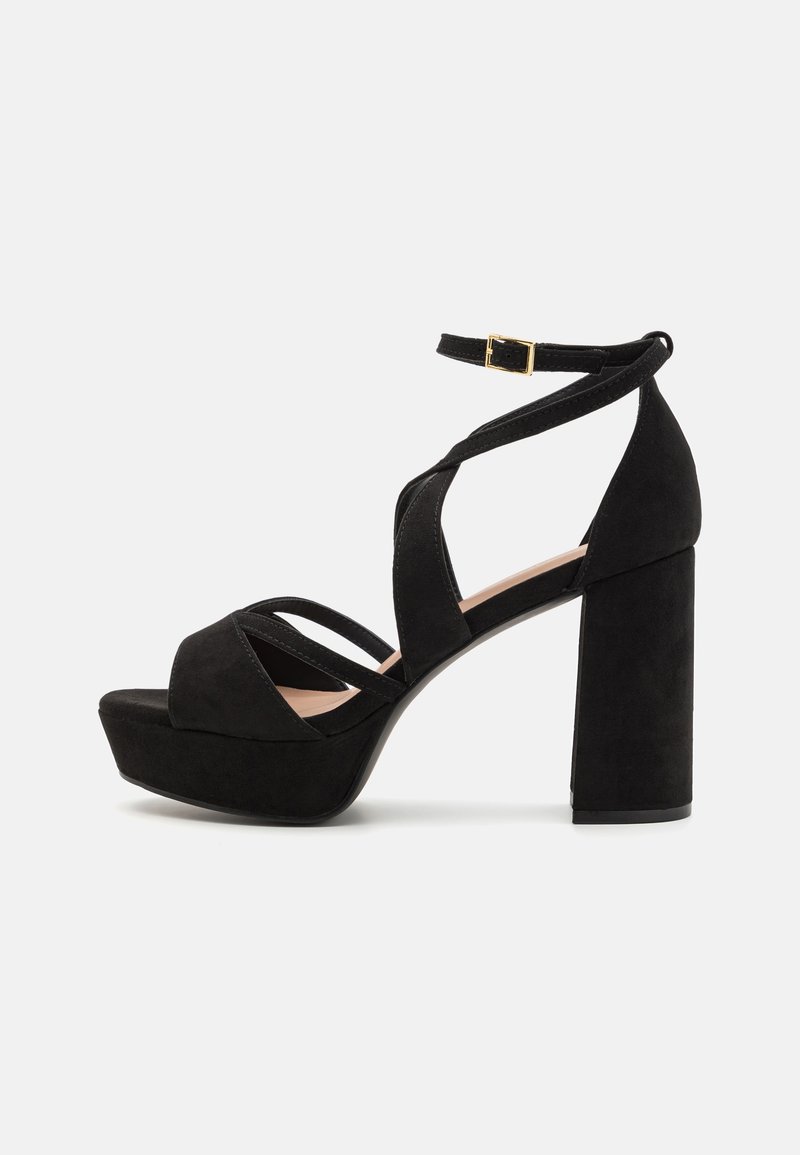 Black suede platform sandals with a chunky heel, featuring interlaced straps and a buckle ankle strap. Textured surface and modern design.
