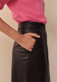 Czarna skórzana spódnica z dopasowaną talią i boczną kieszenią, zestawiona z jasnoróżowym swetrem. Widoczna jest gładka faktura i czyste linie.