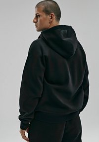 Czarna bluza z kapturem ściąganym, z prążkowanymi mankietami i dołem. Teksturalna tkanina, minimalistyczny design oraz detal z logo przy dekolcie.