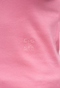 Tela acanalada rosa con la palabra "CLOSED" bordada en un tono claro, ubicada hacia la esquina inferior derecha.