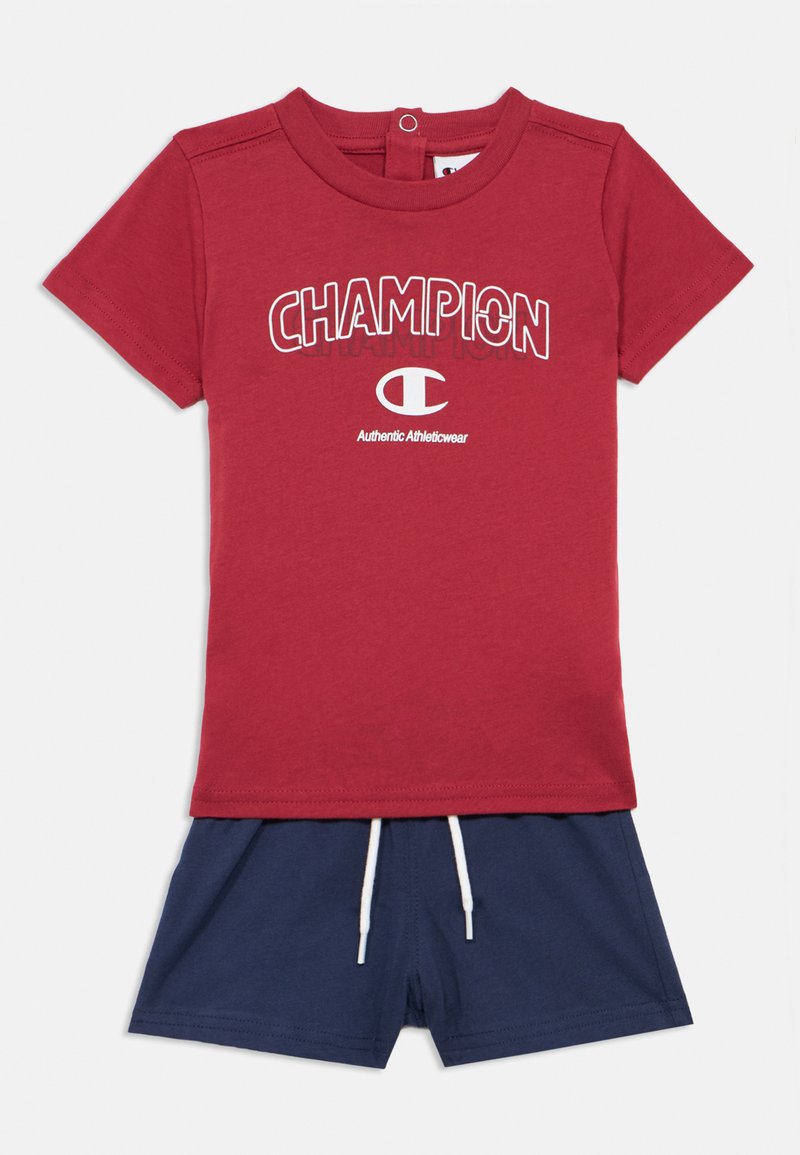 Κόκκινο βαμβακερό t-shirt με λευκό λογότυπο "CHAMPION", συνδυασμένο με ναυτικά σορτς που διαθέτουν ελαστική μέση και λευκή κορδόνι.