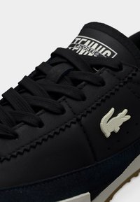 Baskets en cuir noir avec des accents en daim texturé bleu marine, bout arrondi, lacets plats noirs et détail de logo blanc sur la langue et le côté.