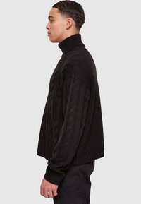Maglione a collo alto in maglia nera, con una vestibilità morbida, caratterizzato da polsini a coste e un motivo testurizzato lungo le maniche.