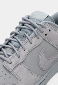 Lys grå semsket skinn sneakers med flate snørebånd, en polstret tunge og et teksturert swoosh-logo. Har perforeringer og forsterkede søm detaljer.