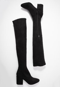 Bottes noires au-dessus du genou en suède doux, avec un bout rond, un talon épais et une fermeture éclair latérale pour un enfilage facile. Texture lisse sur toute la surface.