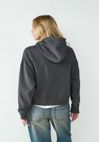 Przycięta, ciemnoszara bluza z dużym kapturem i ściągaczem, w połączeniu z jasnoniebieskimi, luźnymi dżinsami. Gładka tekstura i swobodny styl.