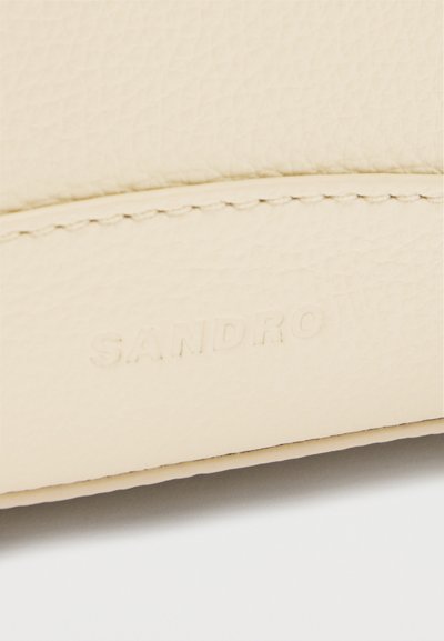 Gros plan sur un cuir beige texturé avec des coutures détaillées et un logo "SANDRO" embossé discrètement.