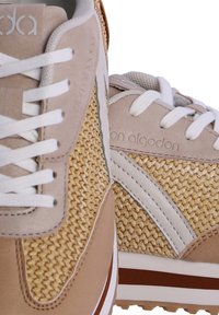 Zapatillas en tonos beige y arena con parte superior de tejido trenzado, cordones blancos y detalles en cuero beige. Presentan una suela texturizada y un discreto detalle de marca.