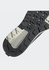 Schwarze Gummi-Schuhsohle mit strukturierten Griffen und gemusterten Rillen, mit grauen Akzenten und einem Logo auf einem hellgrauen Abschnitt.