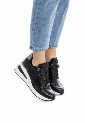 Zapatillas altas de cuero negro con suela blanca, que presentan cordones frontales y un zipper lateral, acentuadas con un sutil patrón texturizado.