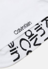 Baltos kojinės su juodu "Calvin Klein" logotipu ir abstrakčiais juodais raštais. Pagamintos iš minkštos medžiagos su glotnia tekstūra.