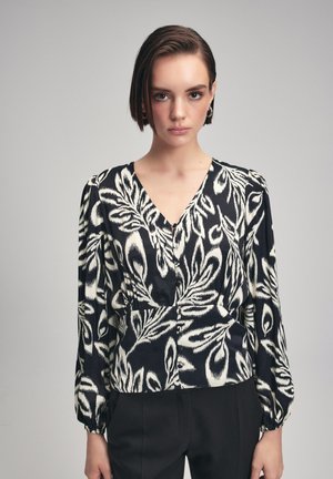 Schwarz-weiße gemusterte Bluse mit V-Ausschnitt, langen Puffärmeln und Knopfdetails, mit einem abstrakten Blättermuster auf glattem Stoff.