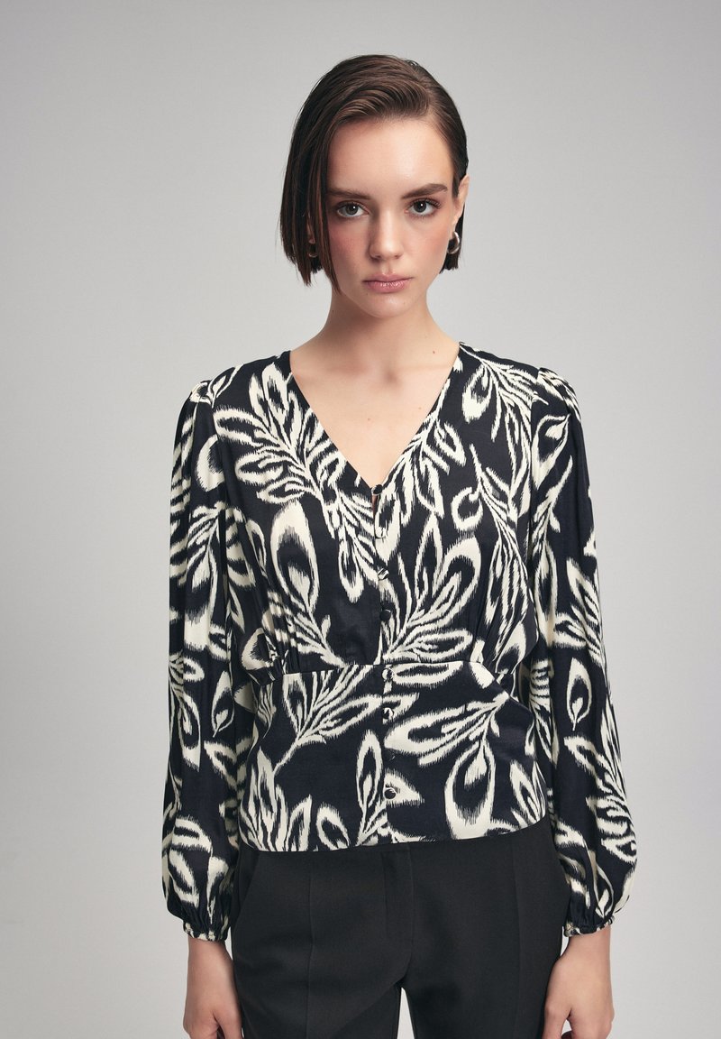 Zwart-wit gebloemde blouse met een V-hals, lange pofmouwen en knoopdetail, met een abstract bladmotief op een gladde stof.