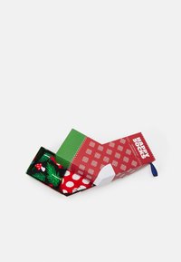 Dva páry ponožek v zelené a červené krabičce s vánočním motivem. Jedna ponožka má černý základ s zeleným listím a červenými bobulemi, druhá je červená s bílými puntíky.