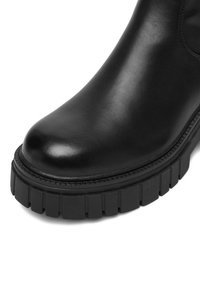 Czarne skórzane botki za kostkę z okrągłym noskiem i grubą, żłobioną czarną gumową podeszwą. Powierzchnia jest gładka z delikatnym połyskiem.