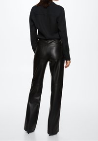 Black leather pants with a high waist, wide leg, and back pockets. Smooth texture and sleek design, paired with a black button-up shirt.