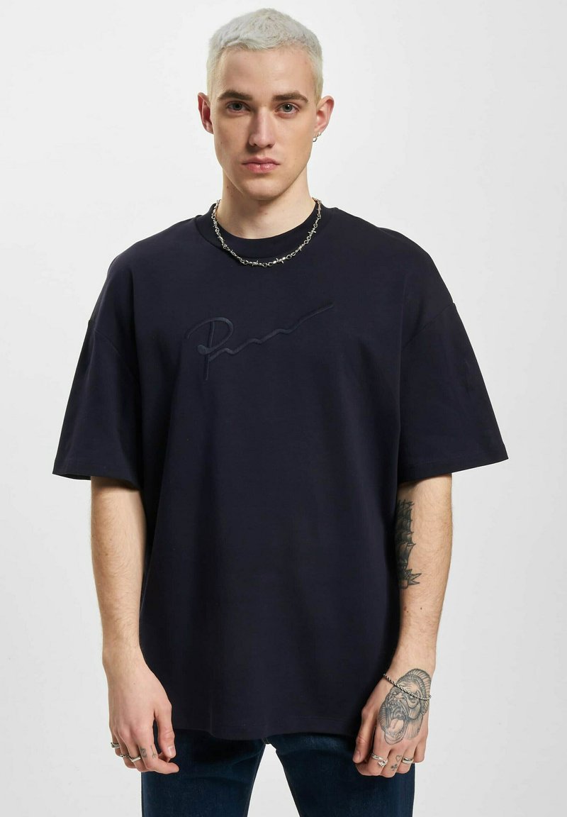 Marineblå oversized t-skjorte med korte ermer, med en tonet brodert signatur på brystet. Laget av bomullsjersey-stoff.