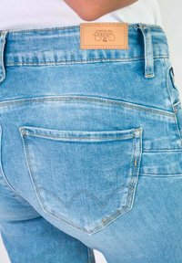 Jean en denim bleu clair avec une étiquette en cuir à la taille. Dispose d'une poche arrière avec un design en zigzag cousu.