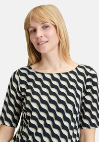 Top wavy w wzory w granatowym, kremowym i zielonym kolorze; okrągły dekolt; krótkie rękawy; gładki materiał z delikatnym połyskiem.