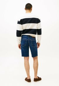 Felpa a righe in bianco e navy, abbinata a pantaloni corti di jeans blu. Dettagli notevoli includono un taglio pulito, con tasche e cuciture visibili.