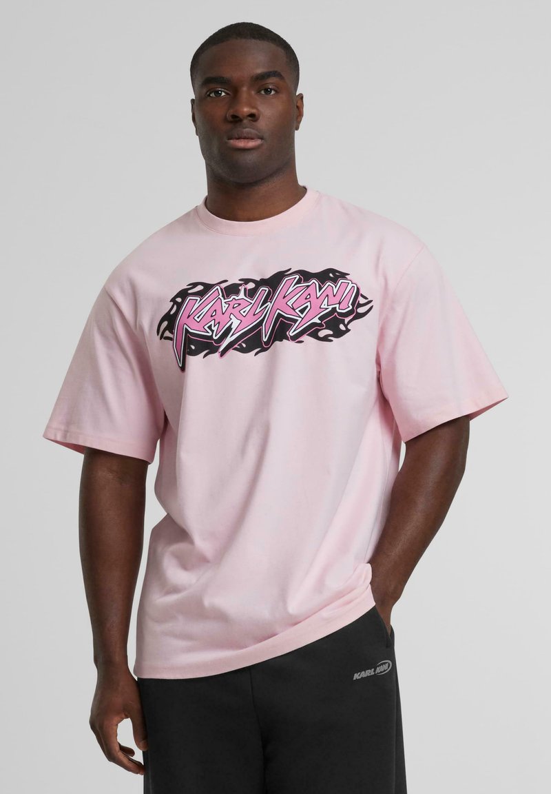 Light pink t-shirt featuring a bold black and pink graphic print, short sleeves, and a round neckline, paired with dark shorts.