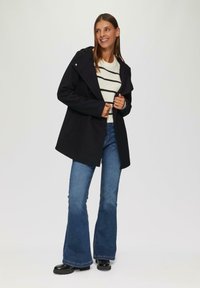 Zwarte jas met een capuchon, dubbelzijdig ontwerp, gecombineerd met een wit gestreept sweater en blauwe flared jeans. Glanzende zwarte laarzen.