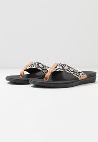 Zwarte flip-flops met gepatterneerde textielbanden met witte geometrische ontwerpen en bruine faux leren accenten, gemonteerd op een zwarte zool.