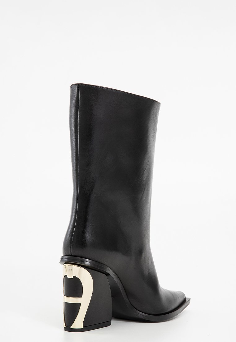 Botte de cheville en cuir noir avec un bout carré, tige plate et un talon bloc sculpté avec un accent logo doré. Texture lisse.